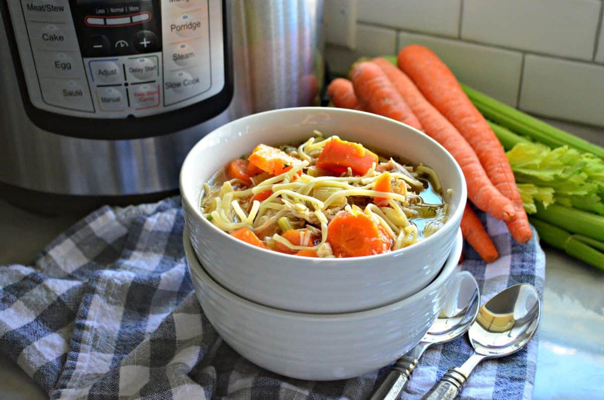 bowl of chicken noodle soup with carrots and celery in it in front of instant pot, carrots, and celery.