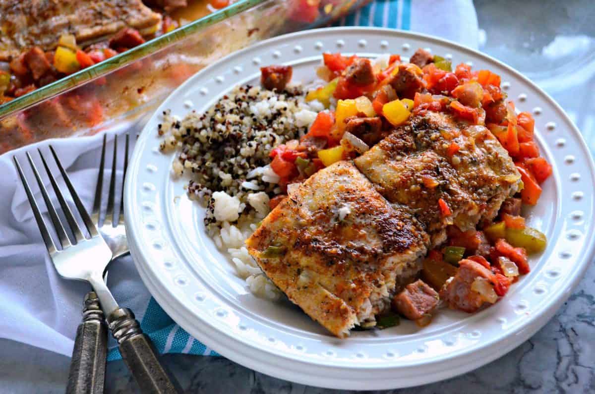 plated baked mahi mahi with chopped veggies and sausage on bed of rice and quinoa with forks.