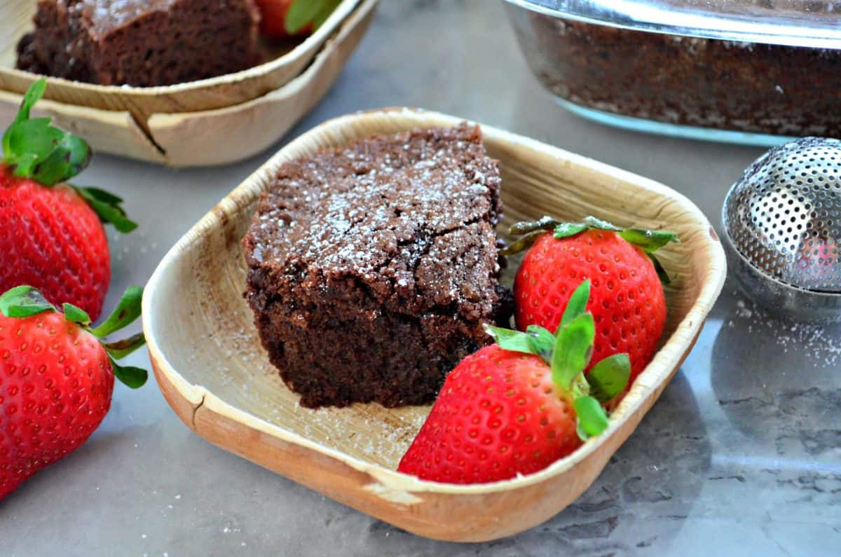 square bowl with slice of chocolate brownie and fresh strawberries.