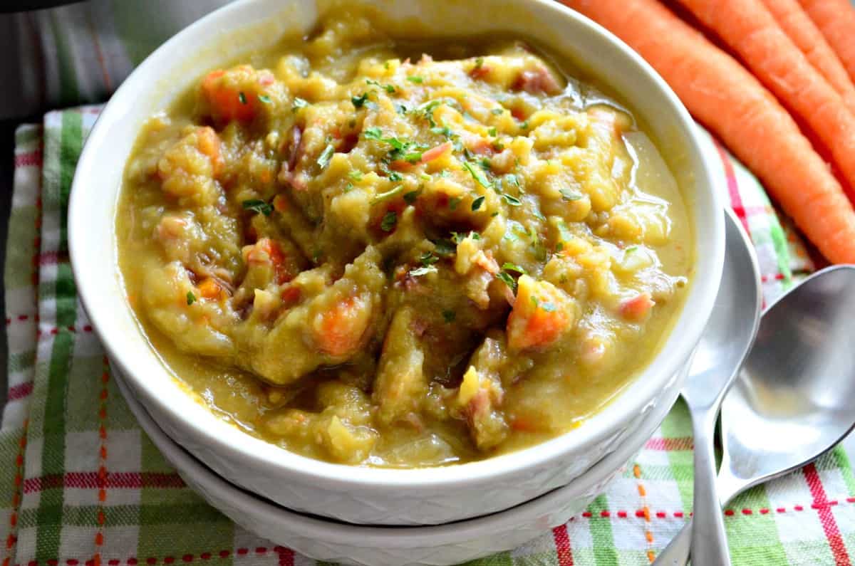 closeup Instant Pot Split Pea & Ham Soup in bowl next to spoons and fresh whole carrots on counter.