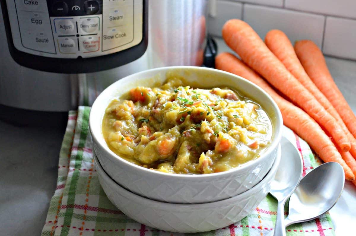 Instant Pot Split Pea & Ham Soup in bowl next to spoons and fresh whole carrots on counter.