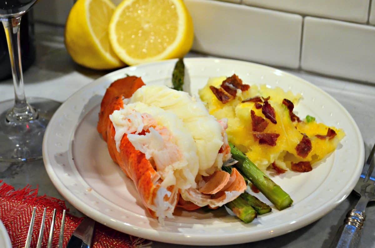 plated cooked lobster tail with potatoes and asparagus with cut fresh lemon in background.