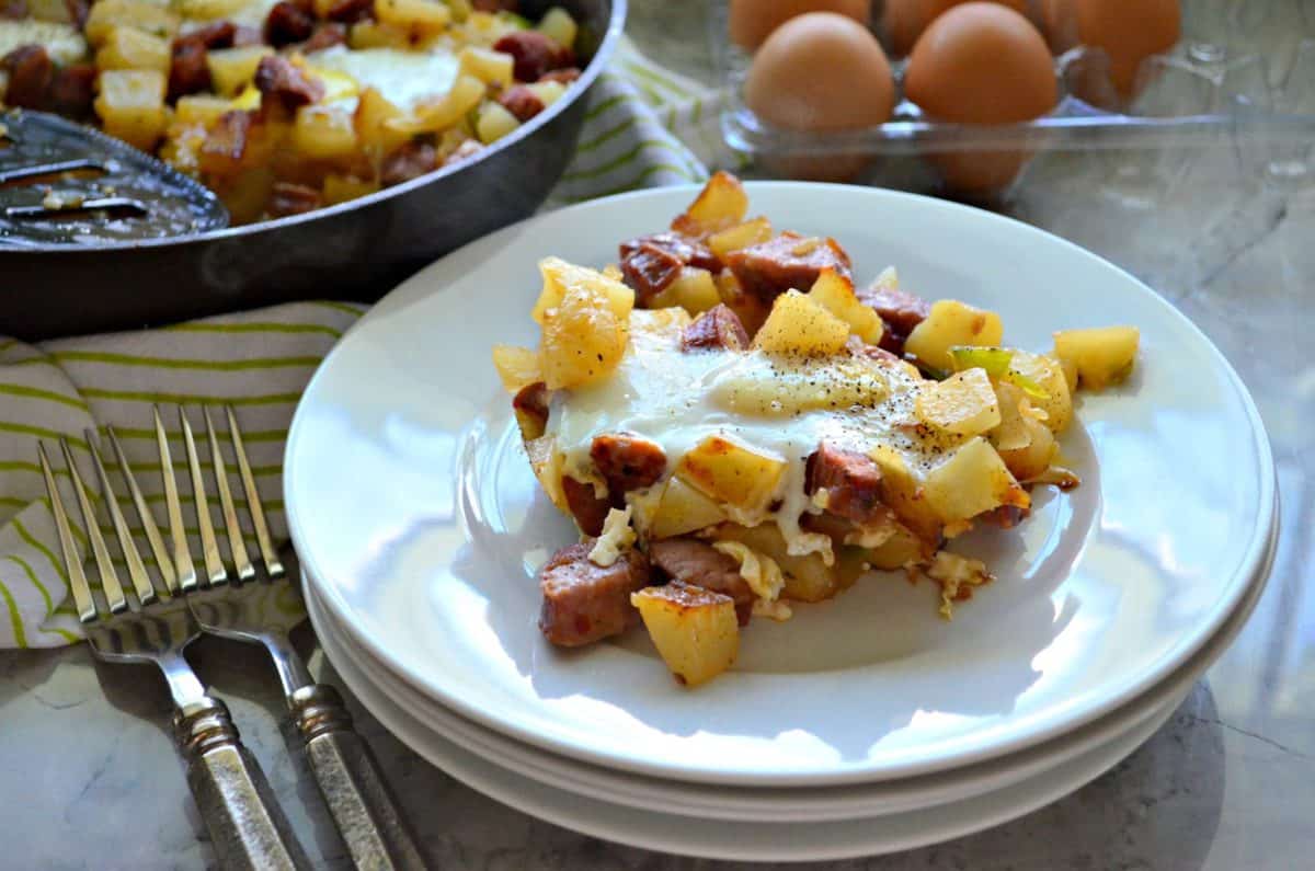 plated diced potatoes, sausage, over easy eggs, peppers on plate next to forks with egg carton in background.