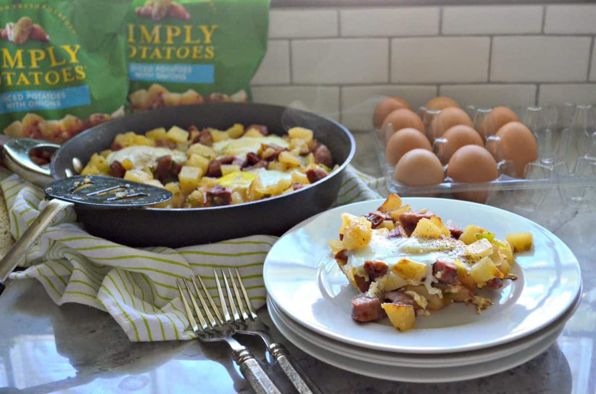 plated diced potatoes, sausage, over easy eggs, peppers, and pepper in front of skillet next to forks.