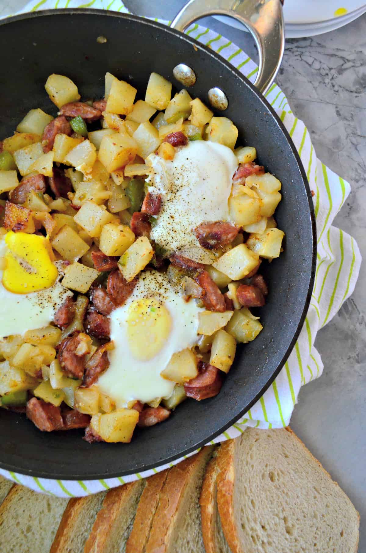 closeup of diced potatoes, sausage, over easy eggs, peppers, and pepper in skillet on counter.