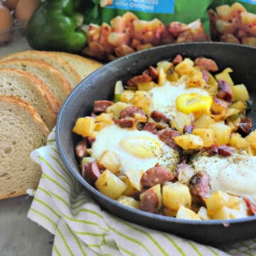 Black skillet filled with eggs, potatoes, and sausage with rye bread on the side.