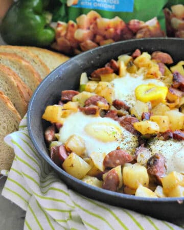 Black skillet filled with eggs, potatoes, and sausage with rye bread on the side.