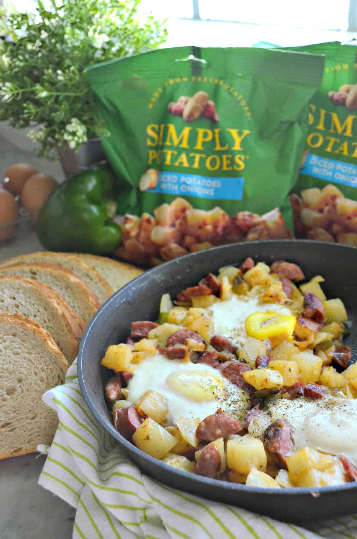 side view of diced potatoes, sausage, over easy eggs, peppers, and pepper in skillet next to toast.