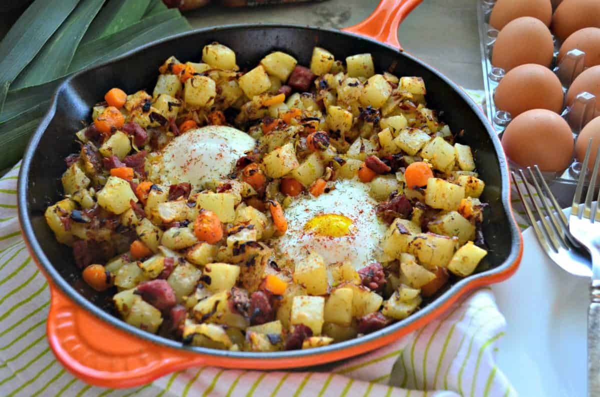 Corned Beef Hash in skillet with overeasy eggs next to egg carton and fresh leek.