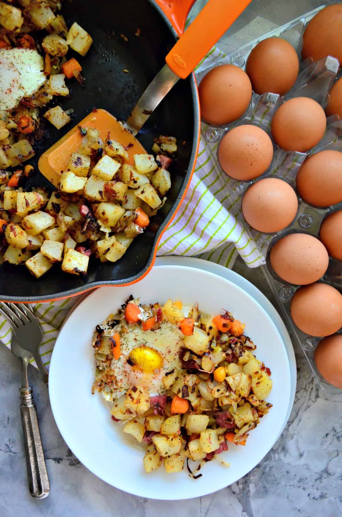 top view plated Corned Beef Hash with overeasy eggs next to egg carton and skillet.