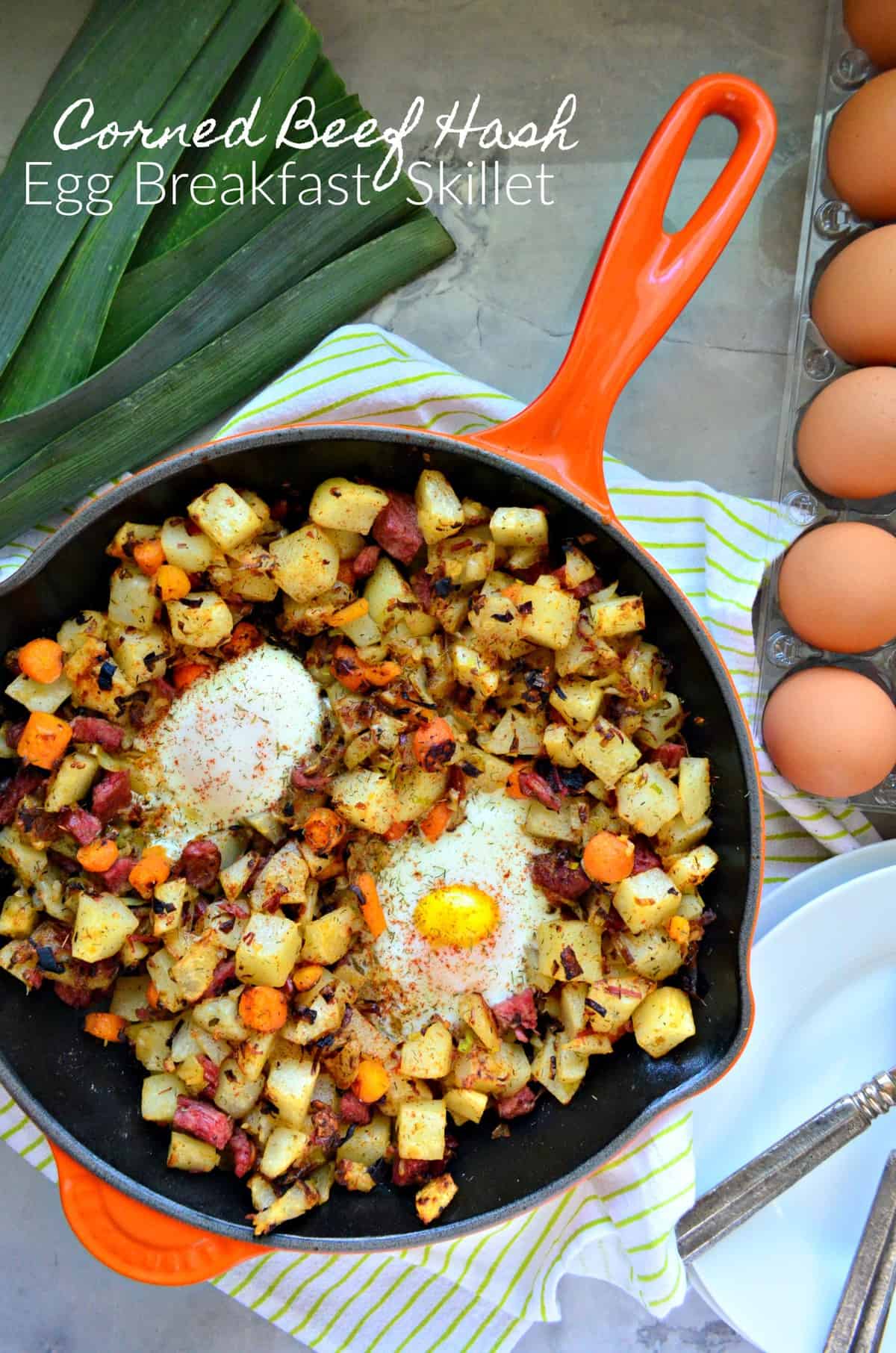top view Corned Beef Hash in skillet with over easy eggs next to egg carton and fresh leek.