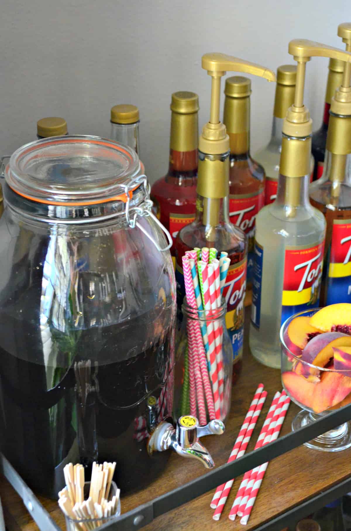 Iced tea on bar cart next to straws and torani syrups.