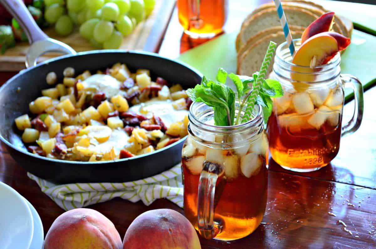 Mint Iced Tea and peach iced tea next to fresh peaches and breakfast skillet on countertop.