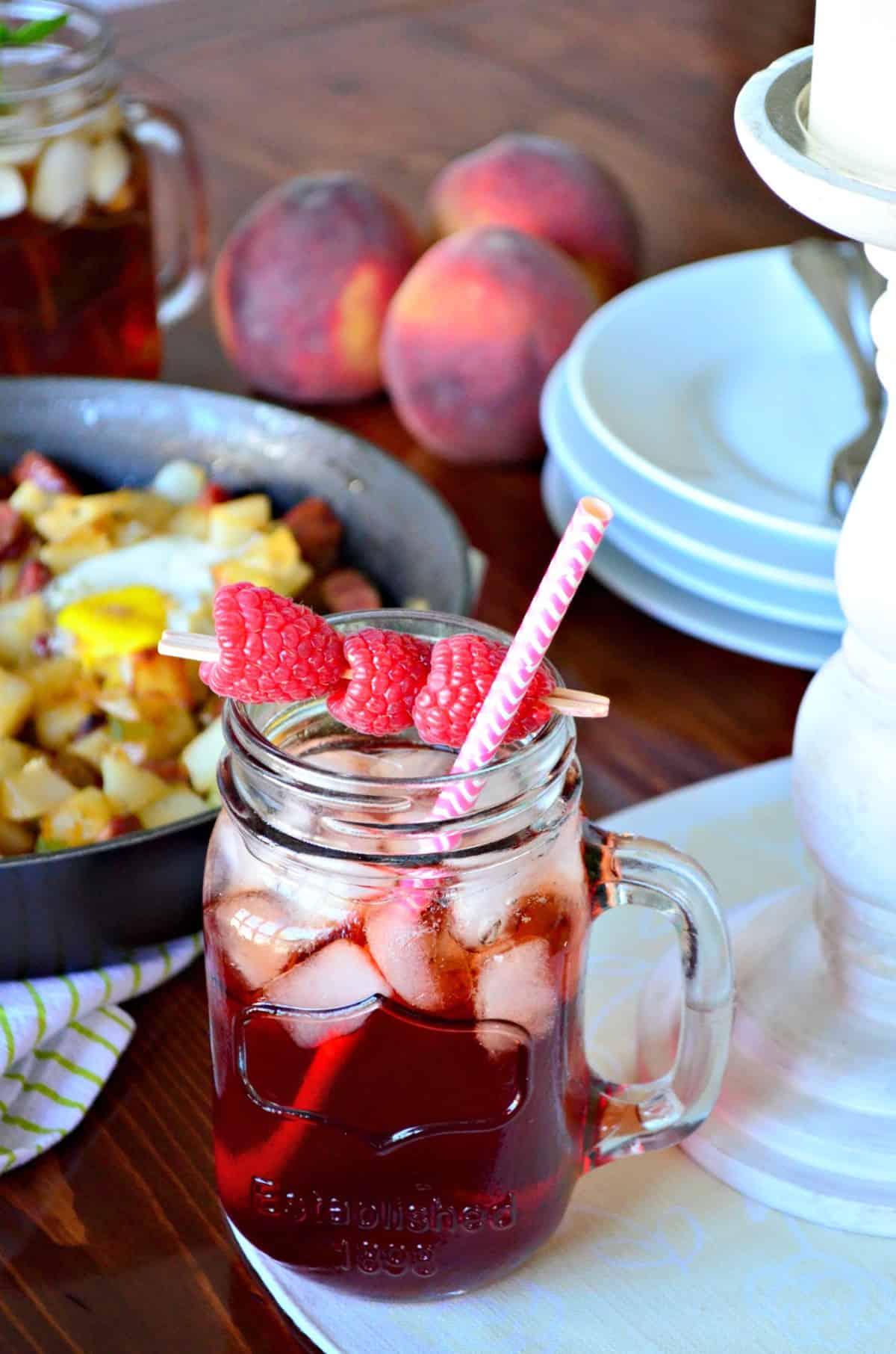 glass jar of iced tea with raspberries skewered on toothpick over top with straws.