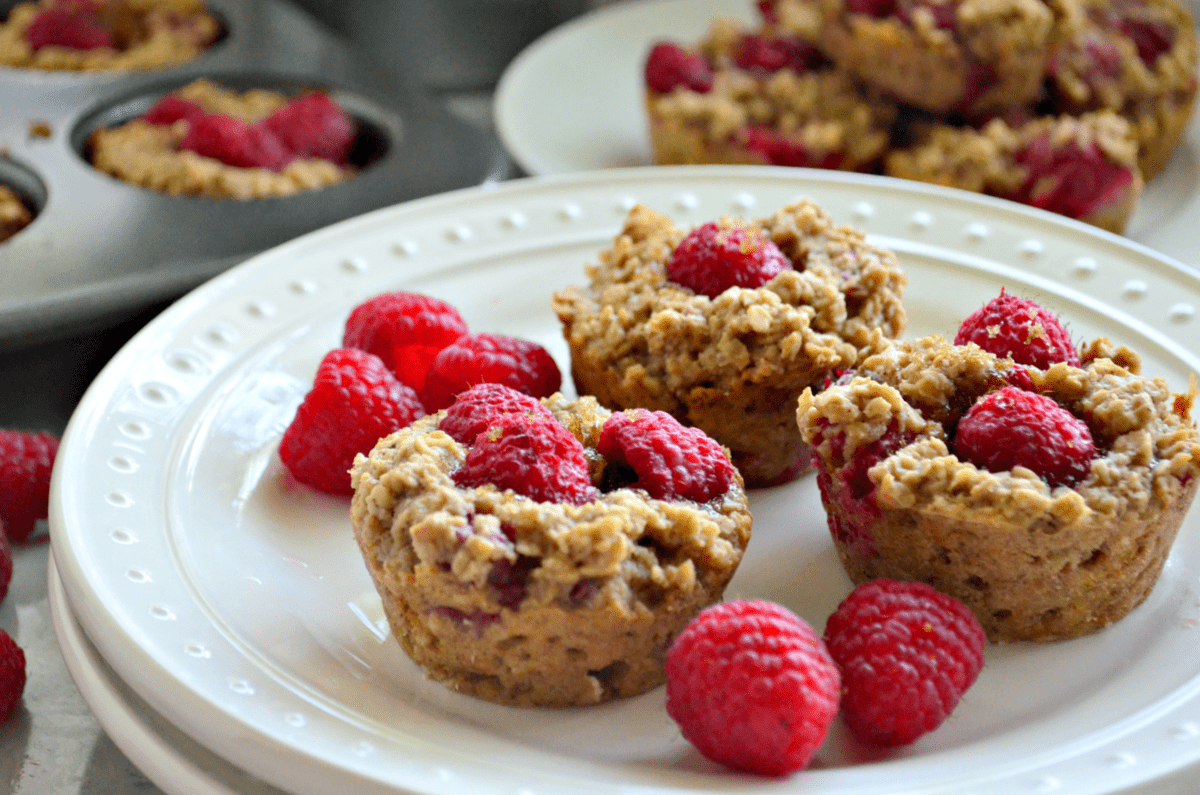 closeup of 3 plated Banana Raspberry Oatmeal Muffins with raspberries on counter.