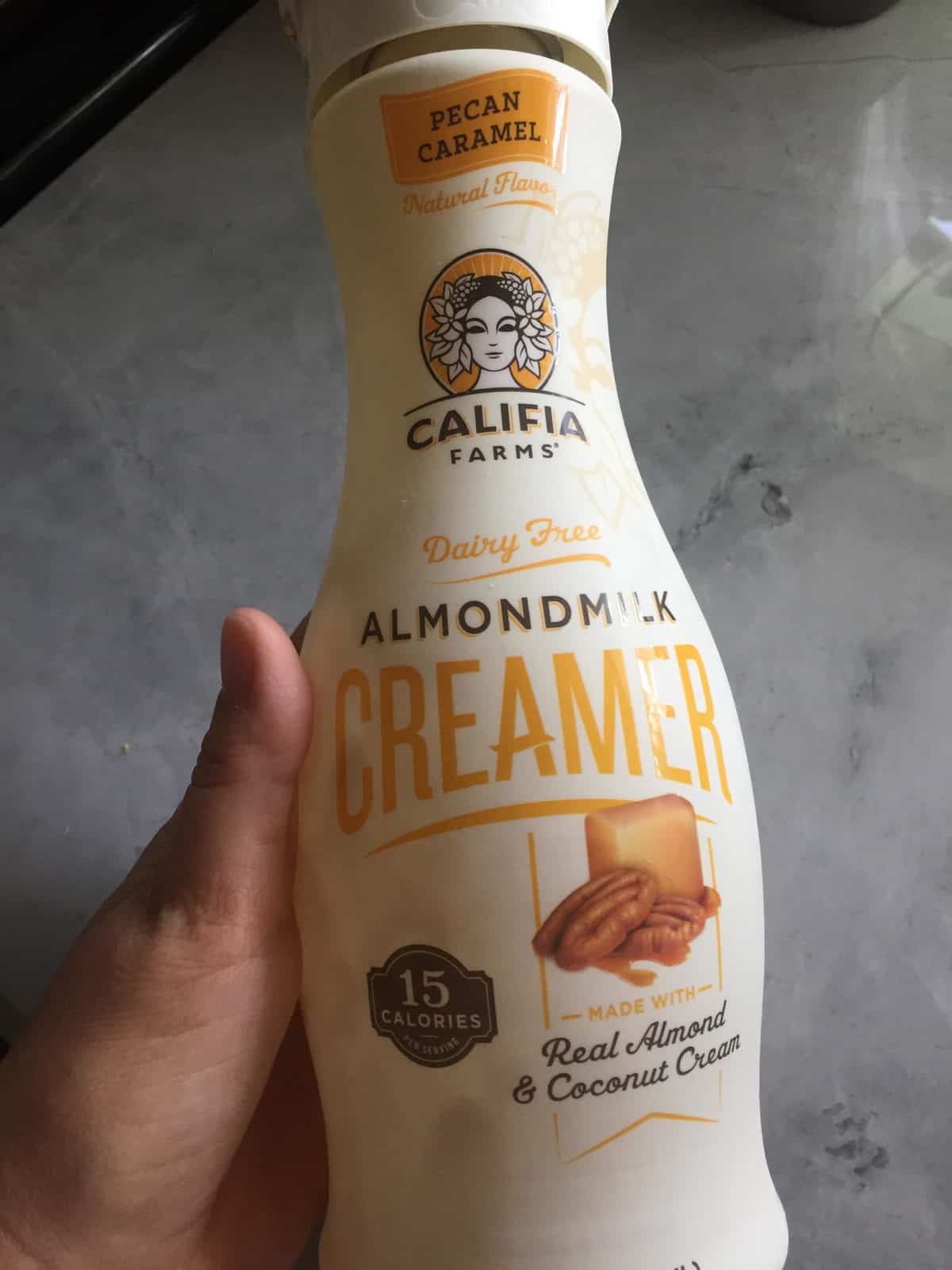 hand holding Dairy Free Creamer - Pecan Carmel Califia Farms Creamer over countertop background.