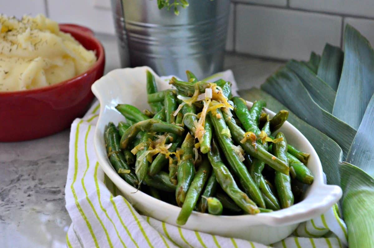 Sauteed Green Beans & Leeks topped with shredded cheese near bowl of mashed potatoes.