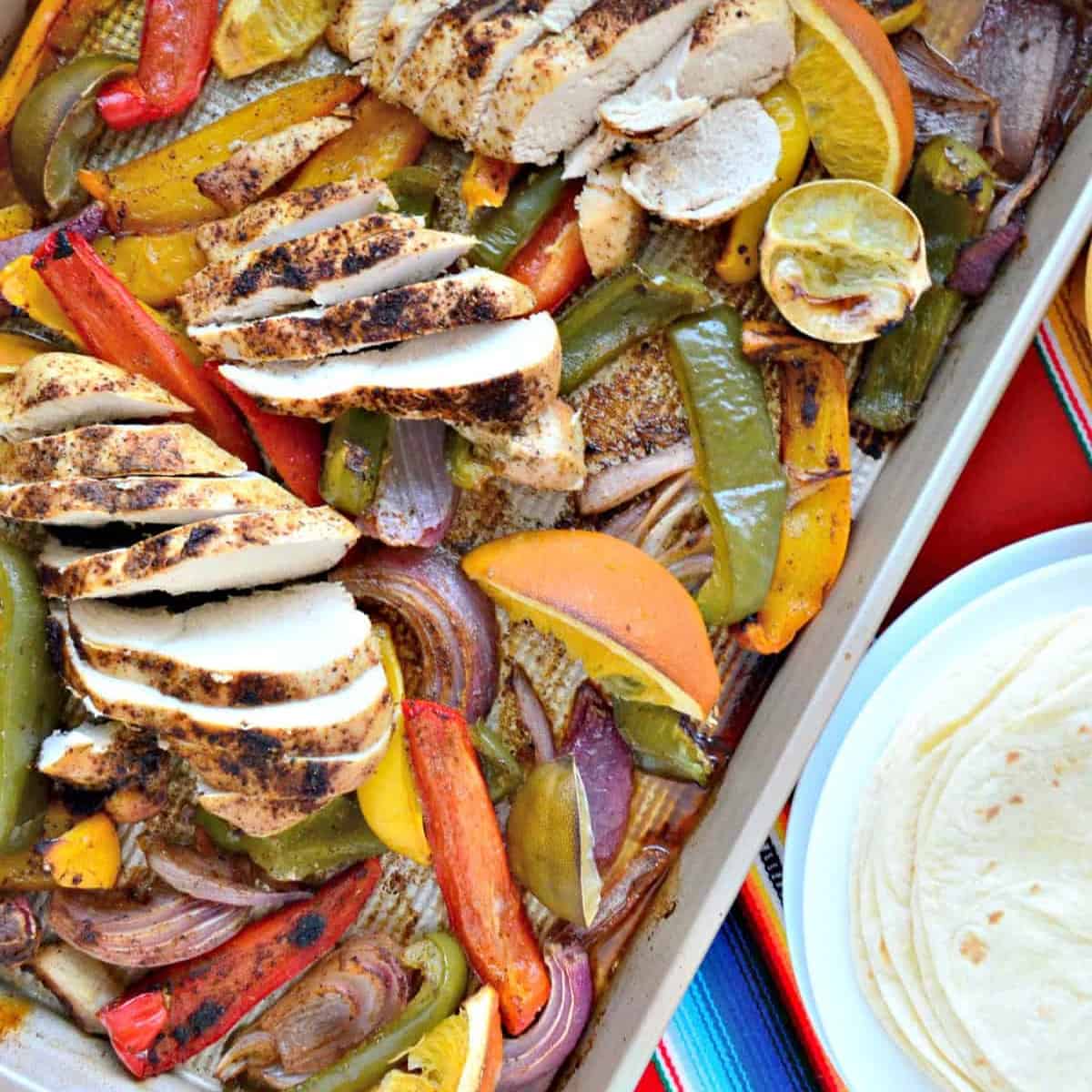 Sheet pan filled with sliced chicken breast, bell peppers, onions, and roasted citrus.