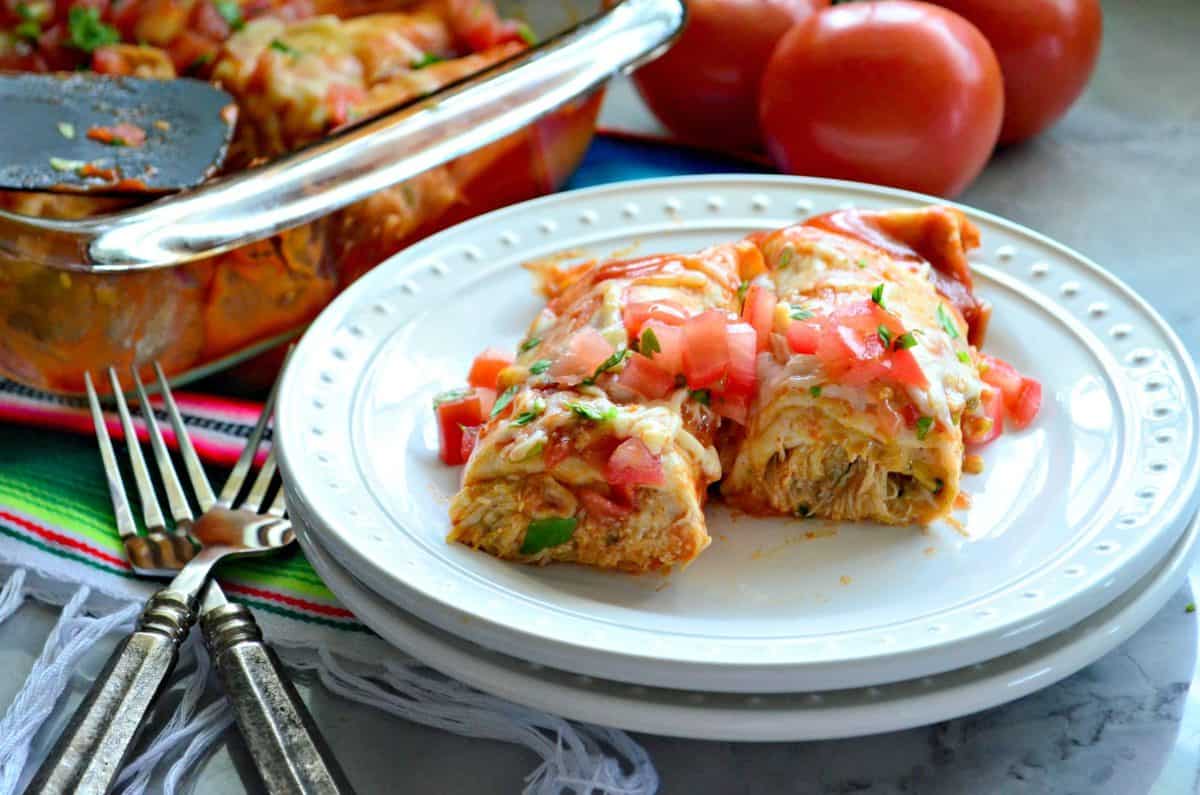 Half of 2 Enchiladas on plate topped with melted cheese, diced tomatoes, and cilantro.