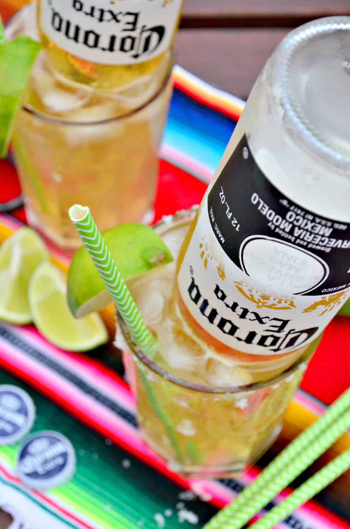 Top view glass of light yellow iced liquid with upside down corona bottle in it on colorful tablecloth.