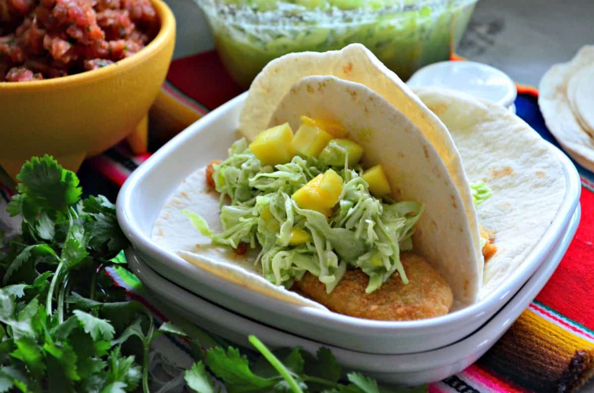 two flour tortilla tacos on a plate with mango coleslaw on it.