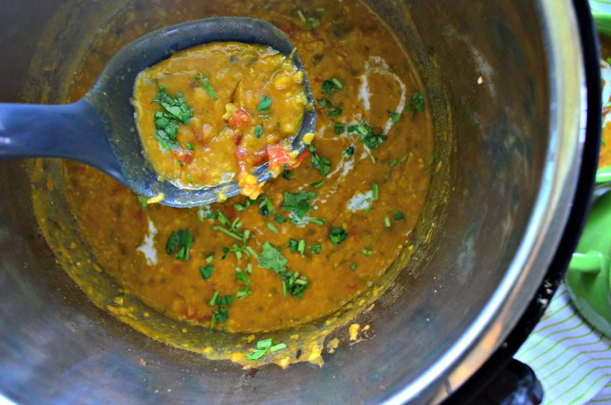 top view of lentils, tomatoes, and herbs in instant pot with spoon.