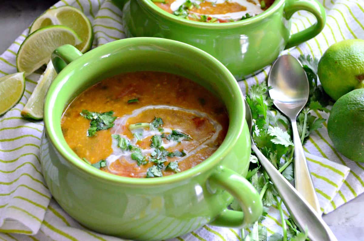 top view of 2 bowls of lentil soup topped with white sauce, and herbs next to spoons.