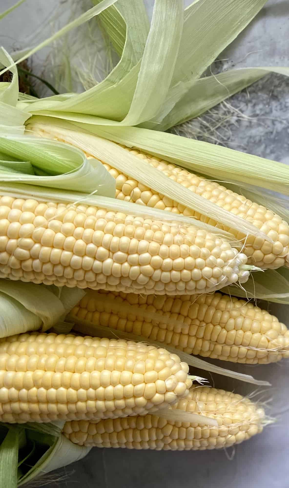 Five ears of corn on the cob on a marble countertop.