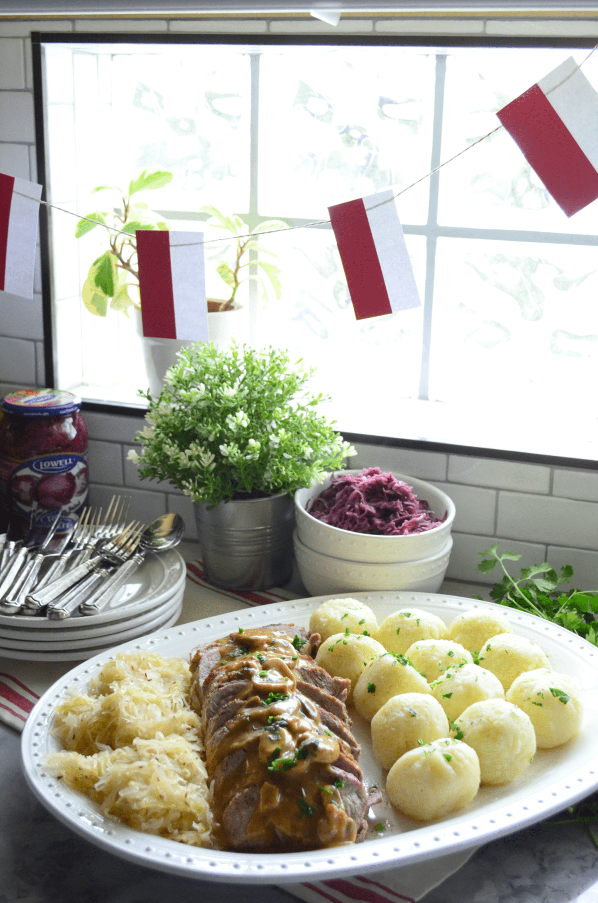 Platter of sauerkraut, roasted pork with gravy, and potato dumplings in front of window.