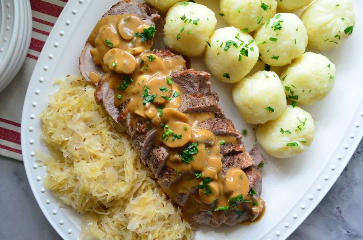 top view platter of sauerkraut, roasted pork with gravy, and potato dumplings in front of window.