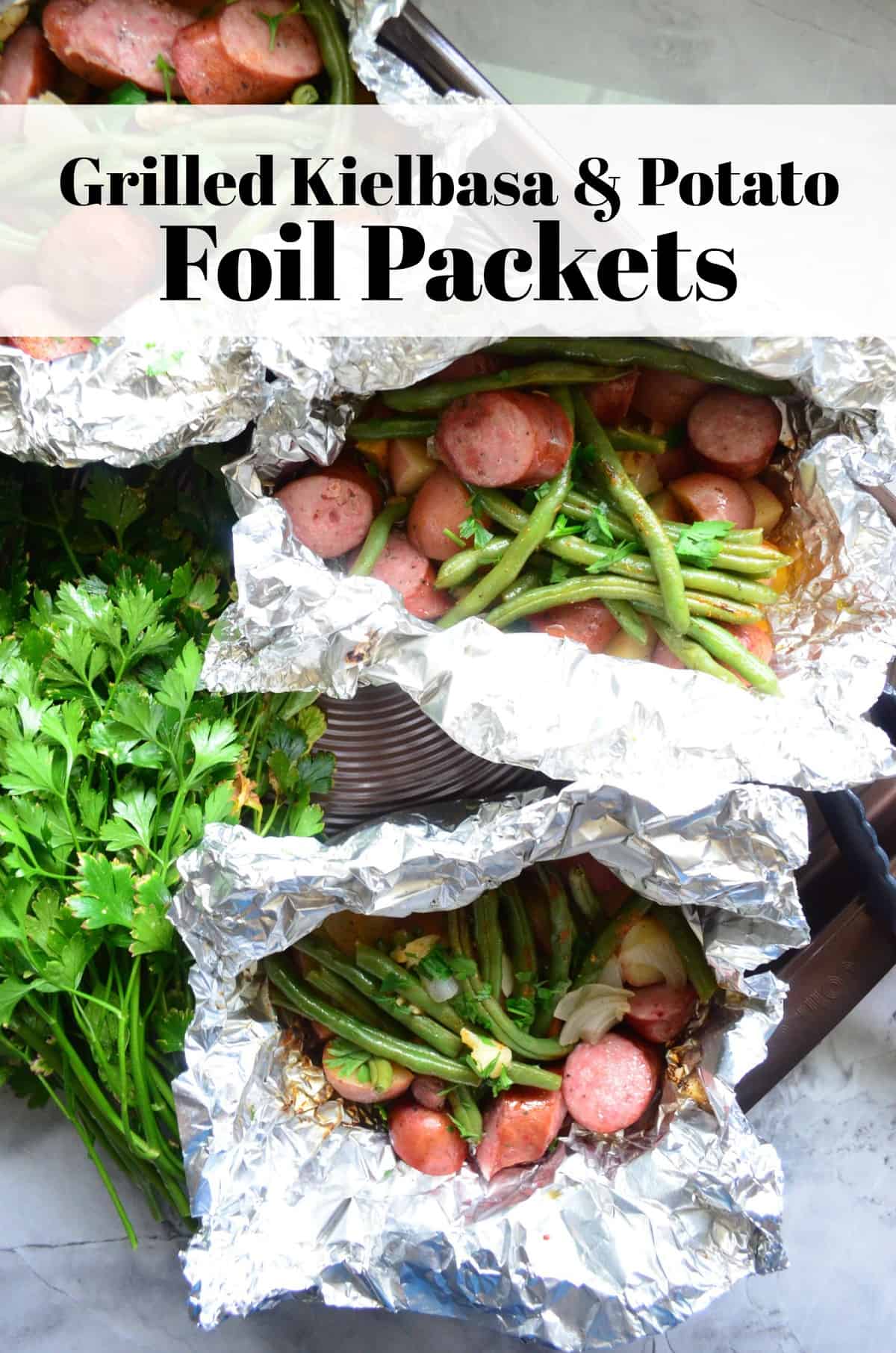 Top view of a sheet pan with foilled packets filled with Kielbasa, Potato, green beans, and parsley with text on image.