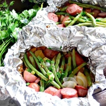 foil packets of kielbasa and green beans next to fresh parsley.