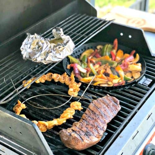 steak, skewered shrimp, bell peppers, and foil packet on grill.