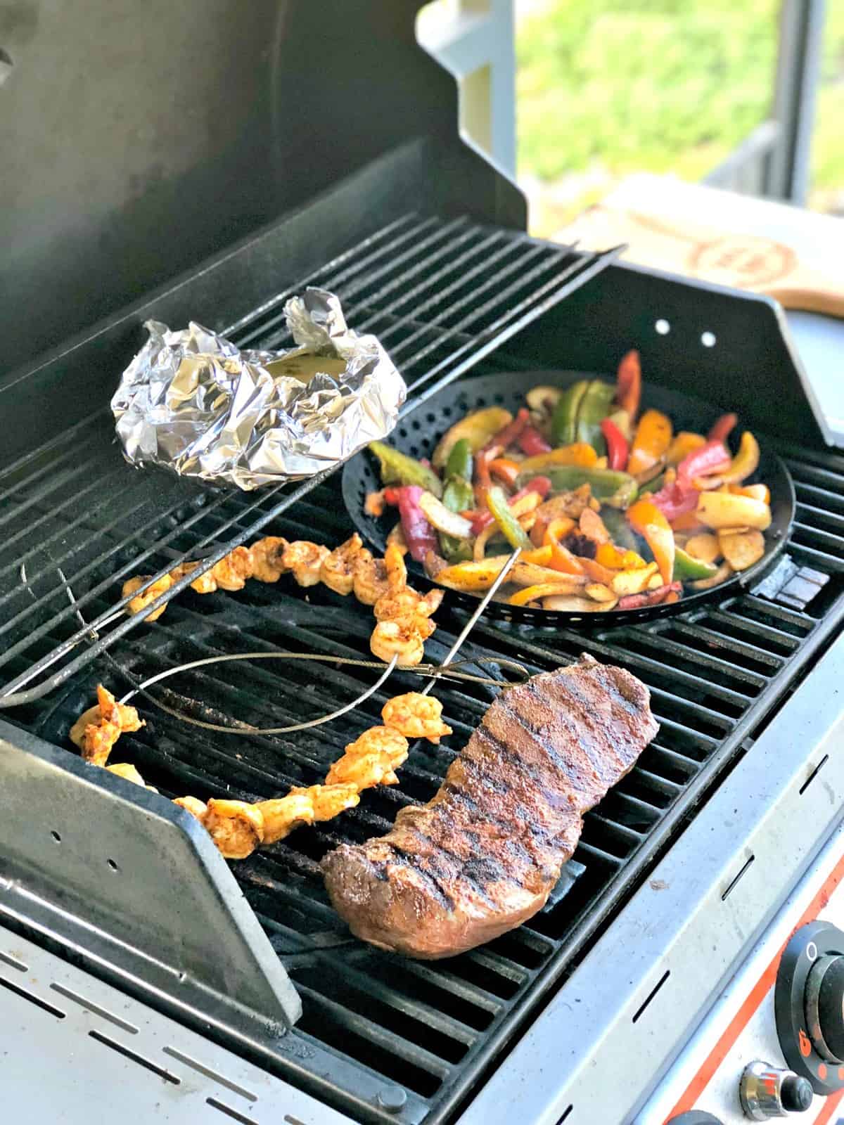 steak, skewered shrimp, bell peppers, and foil packet on grill.