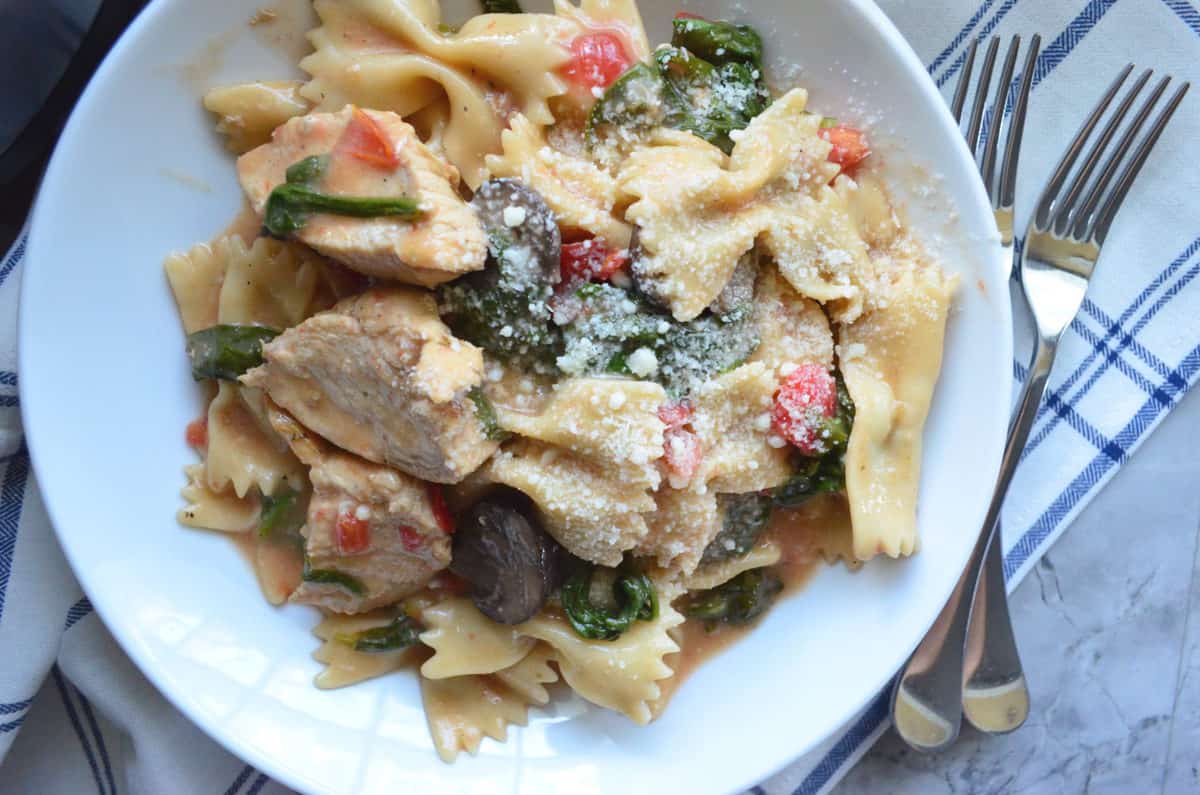 top view of bowl of bowtie pasta with spinach, mushroom, tomato, and cheese.