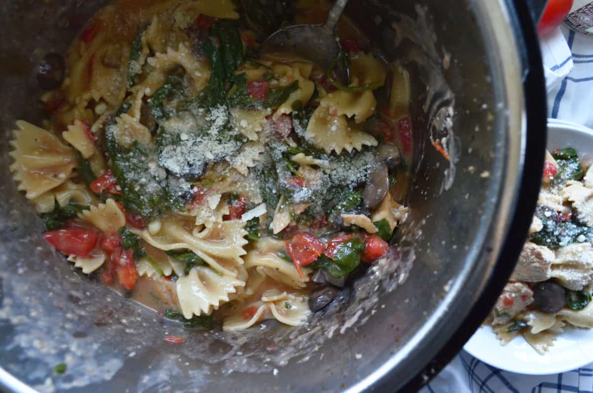 Top view of instant pot filled with tomatoes, mushrooms, spinach, bowtie pasta, and parmesan.