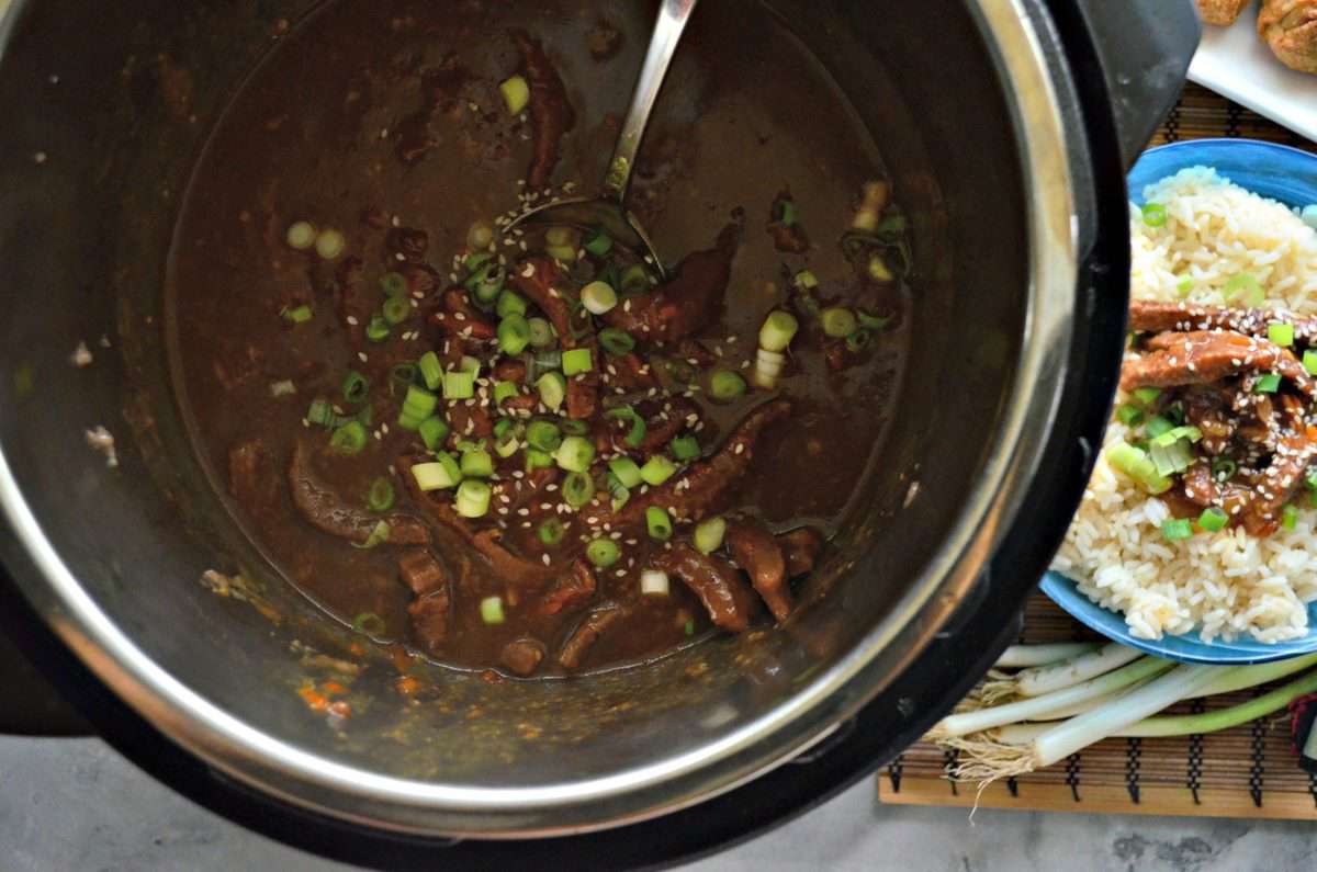 Top view of brown sauce with mongolian beef, green onions, and sesame seeds in instant pot.