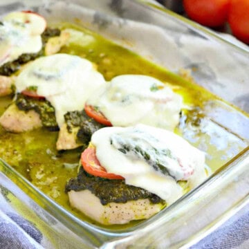 Glass baking dish with chicken, pesto, tomatoes, and cheese.