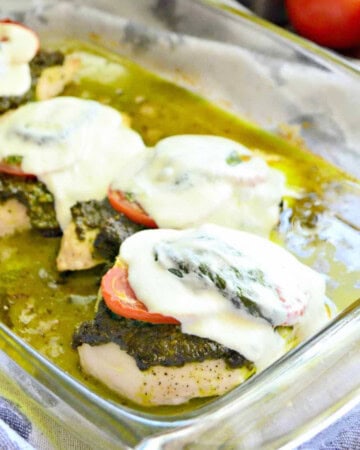 Glass baking dish with chicken, pesto, tomatoes, and cheese.
