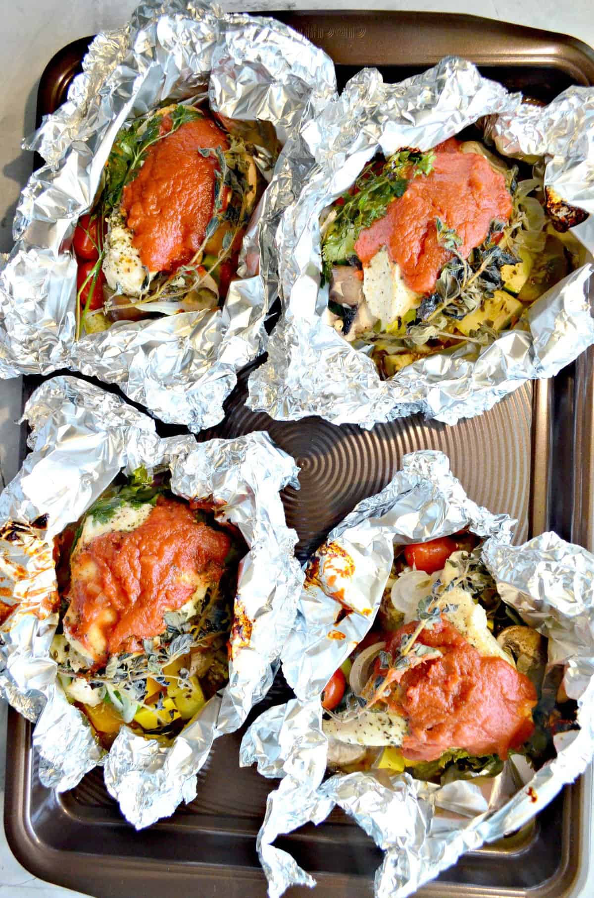 Top view of a brown tray with four foil dinners stuffed with chicken and sauce. 