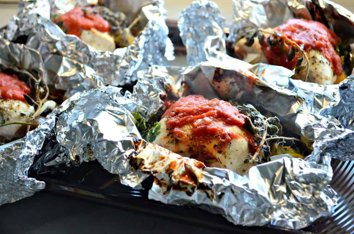 close up of 4 pieces of chicken in an open foil with herbs and red sauce.