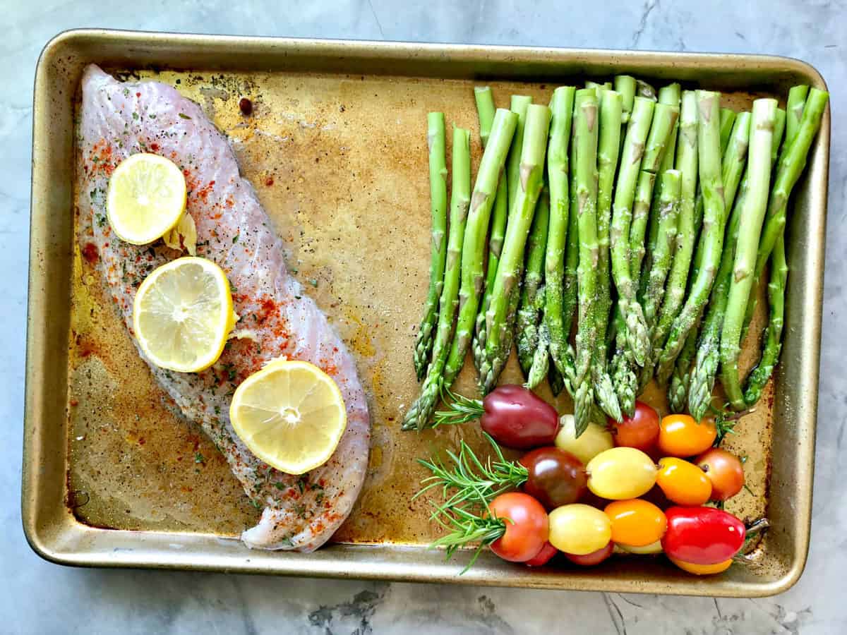 top view baking sheet with uncooked snapper, grape tomatoes, and asparagus.