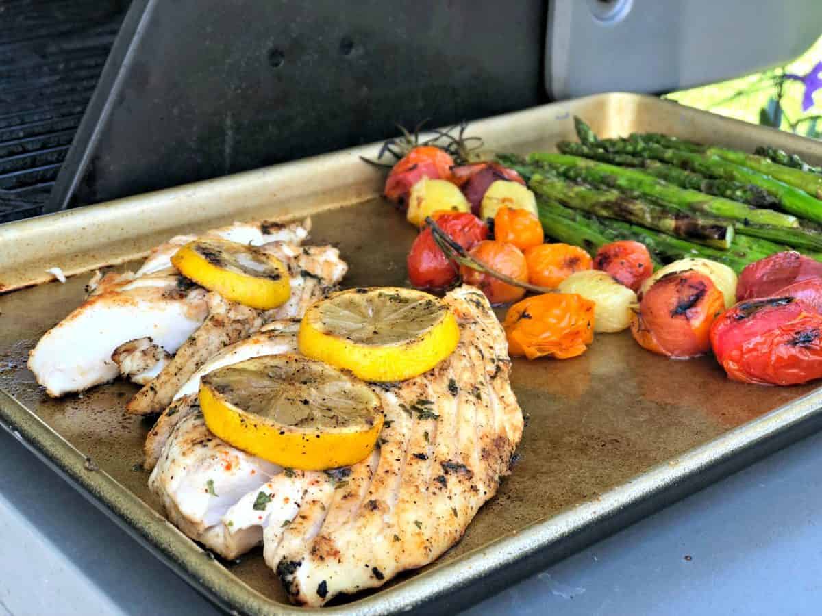 sheet pan with grilled fish topped with lemon wheels, grape tomatoes, and asparagus with title text.