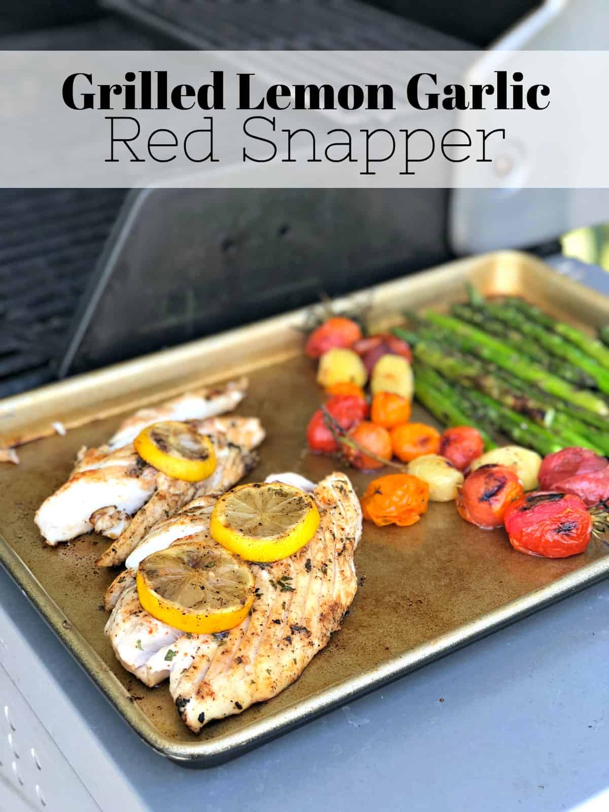 sheet pan with grilled fish topped with lemon wheels, grape tomatoes, and asparagus with title text.