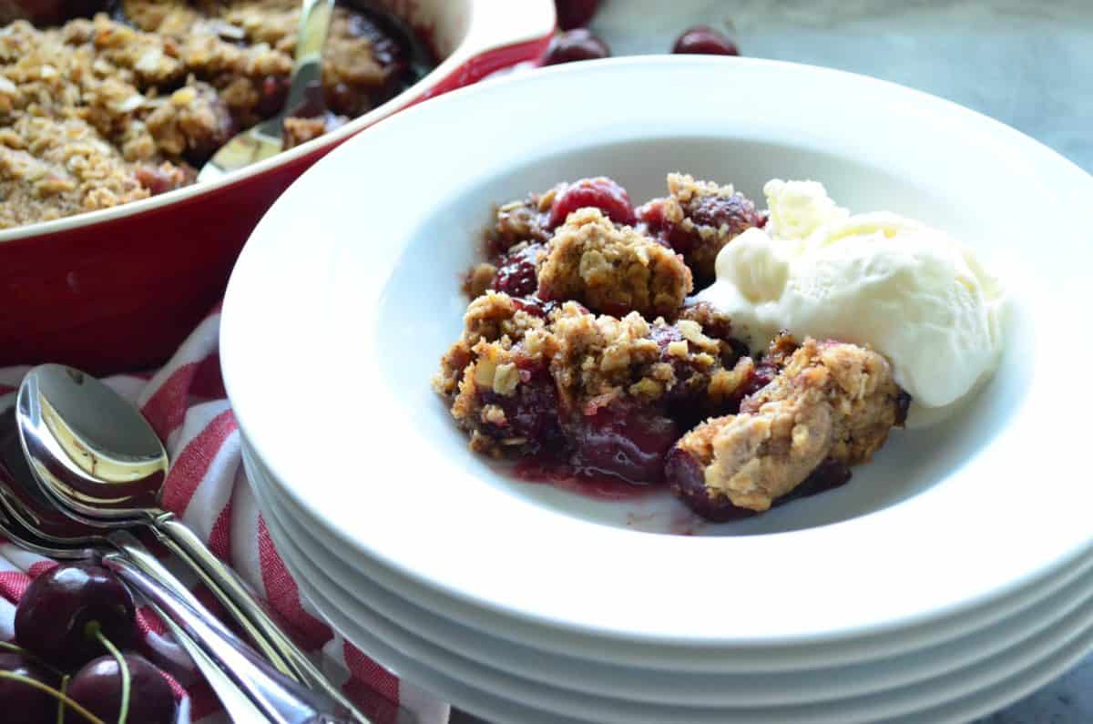 Stack of plates with cherry crisp dessert and scoop of vanilla ice cream on top plate.