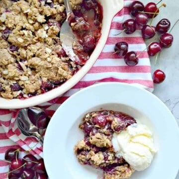 dish with cherries and brown crumbles on top next to plate of dessert with ice cream.