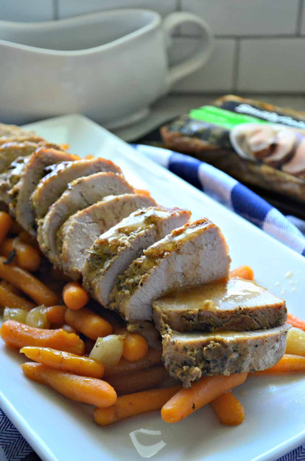 Garlic and Herb Pork Tenderloin with Carrots and Pearl Onions on platter in front of gravy boat.