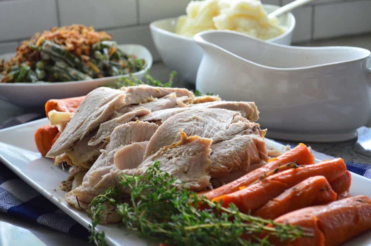 Platter of turkey, carrots, and rosemary in front of mashed potatoes.