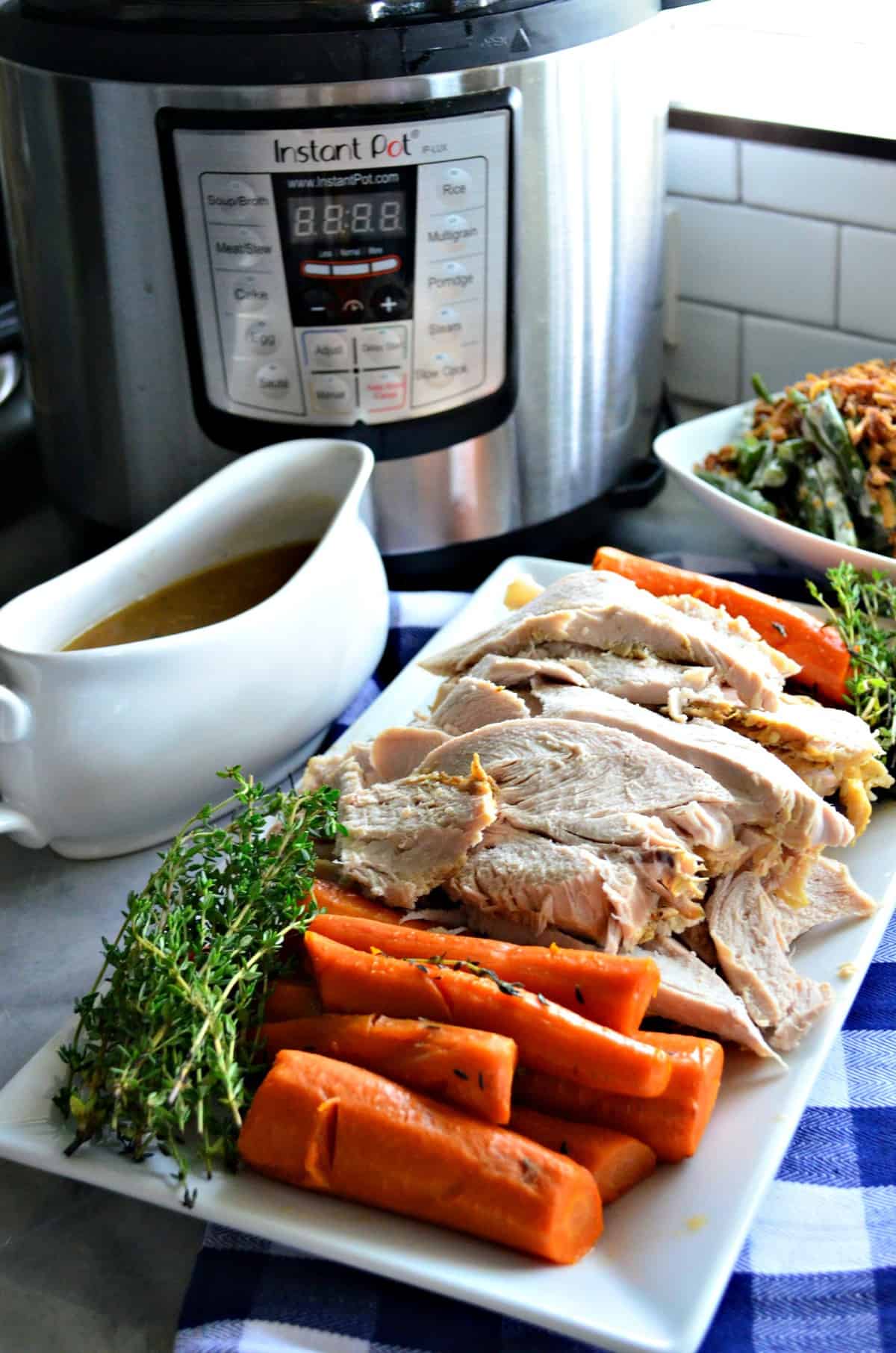 White platter with sliced turkey, carrots, thyme, gravy boat and Instant Pot in background.