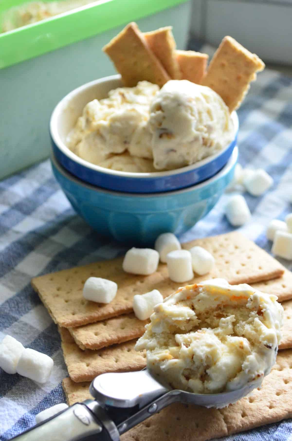 bowl of creamy colored chunky ice cream with graham crackers next to scooper and mini marshmallows.